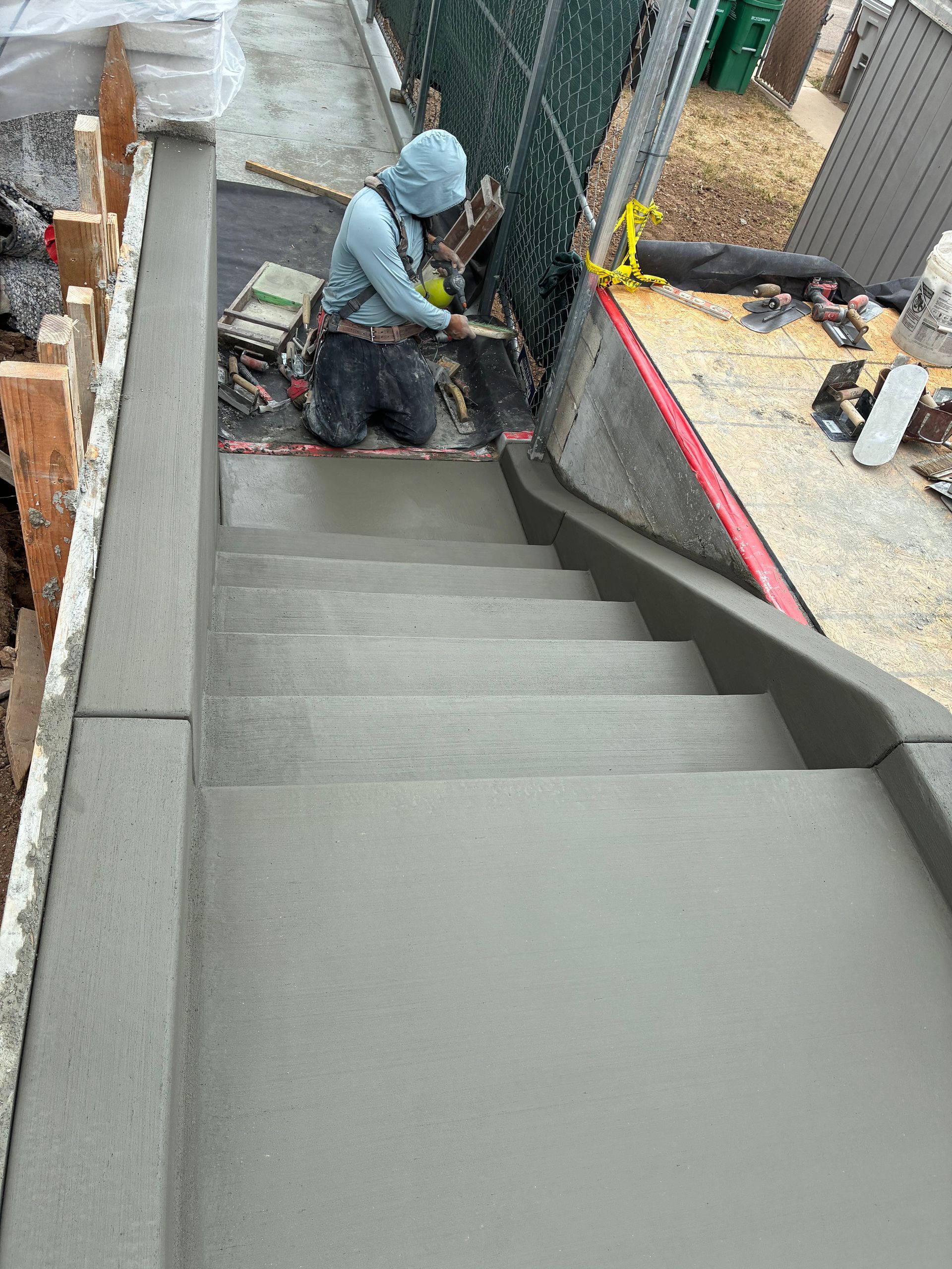 Worker troweling fresh concrete on a stairway beside a construction site