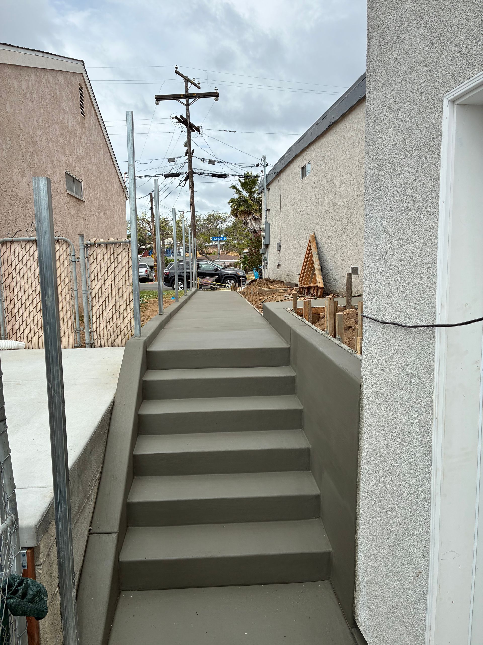 Narrow outdoor stairway between buildings leading up to a street, with utility poles in the background