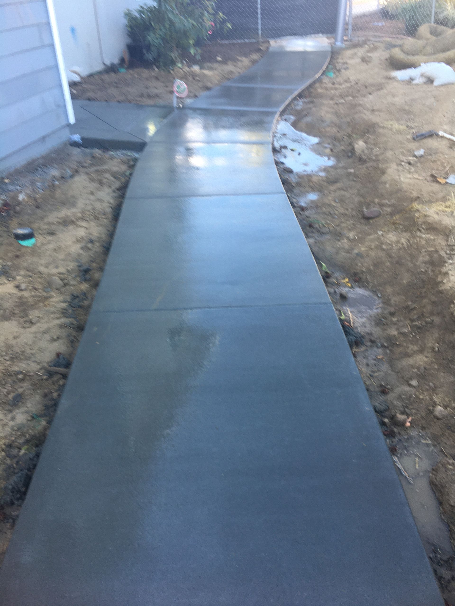 Cracked driveway beside a newly paved blue-gray walkway and green lawn