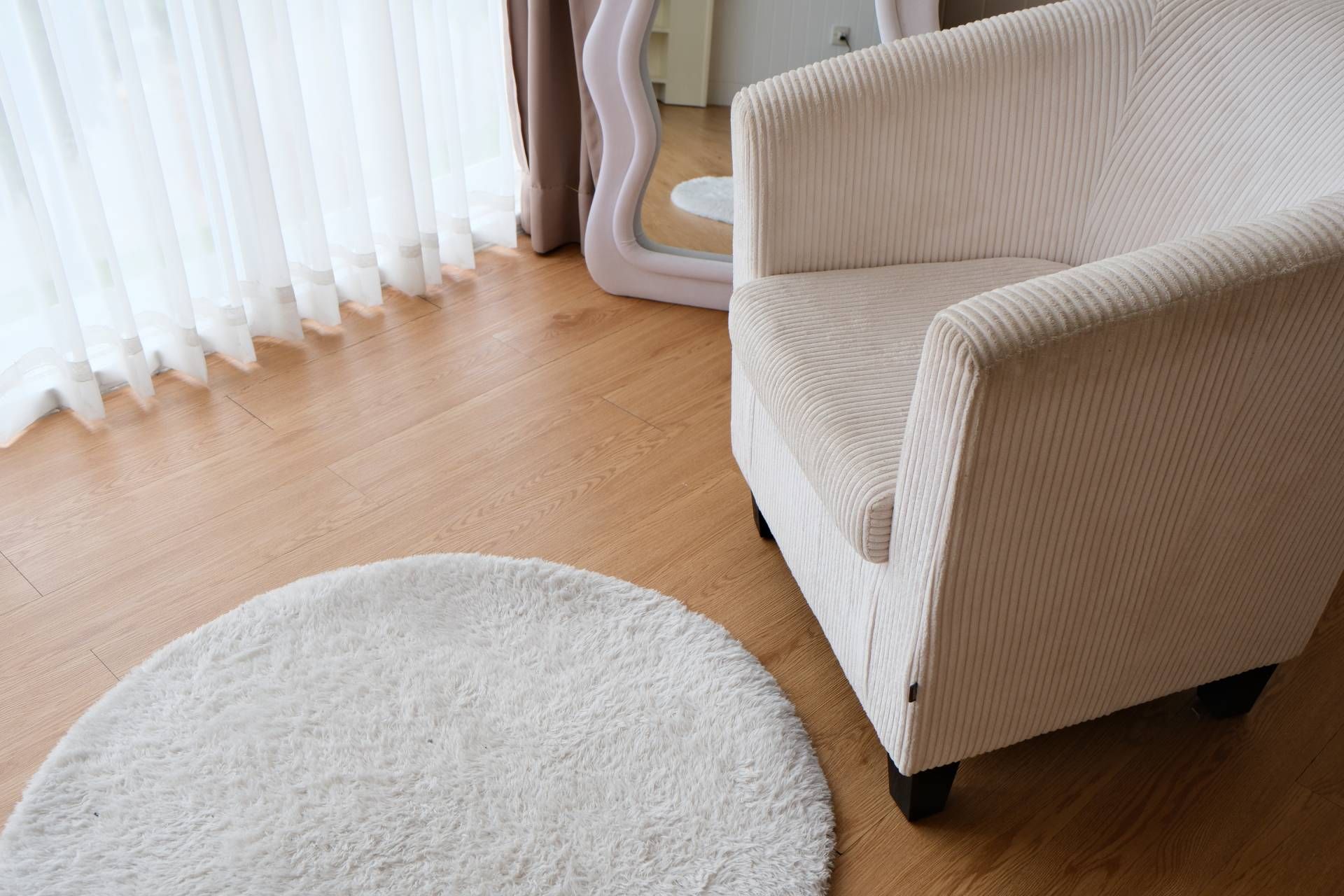 Bright living room with a beige armchair, white rug, and sheer curtains over wooden floor.