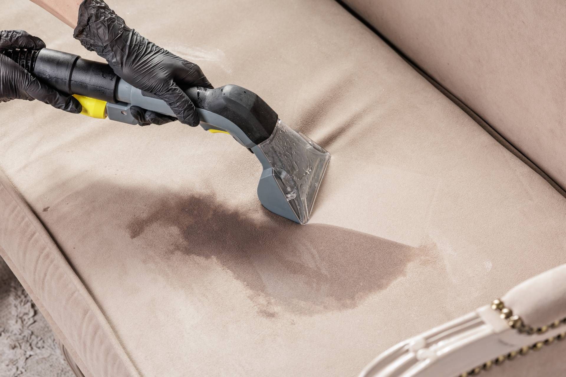 Steam cleaner removing a dark stain from a beige upholstered cushion
