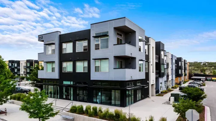 Modern multi-story apartment building with black and light gray exterior walls, large windows, and ground-level storefronts.