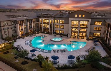 High-angle view of a luxury apartment complex with a central swimming pool and hot tub at sunset.