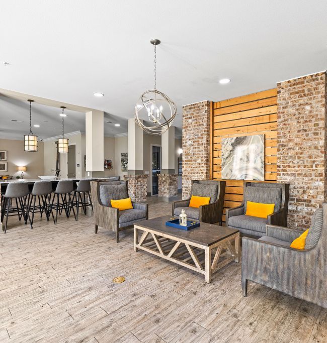 A contemporary lounge with grey armchairs, yellow cushions, a wooden coffee table, and an exposed brick accent wall.