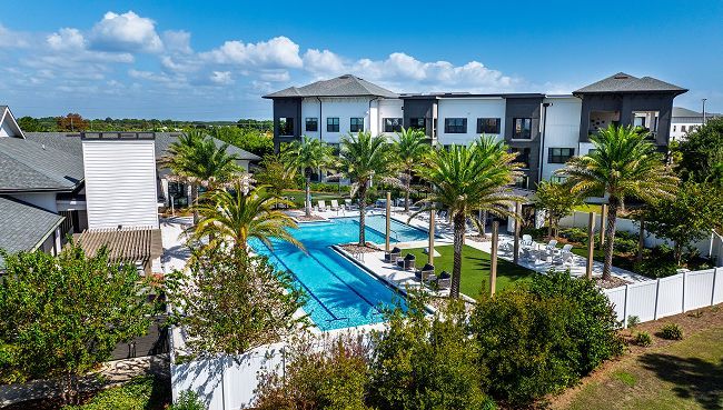 Aerial view of an apartment complex with a rectangular swimming pool surrounded by palm trees and landscaping.