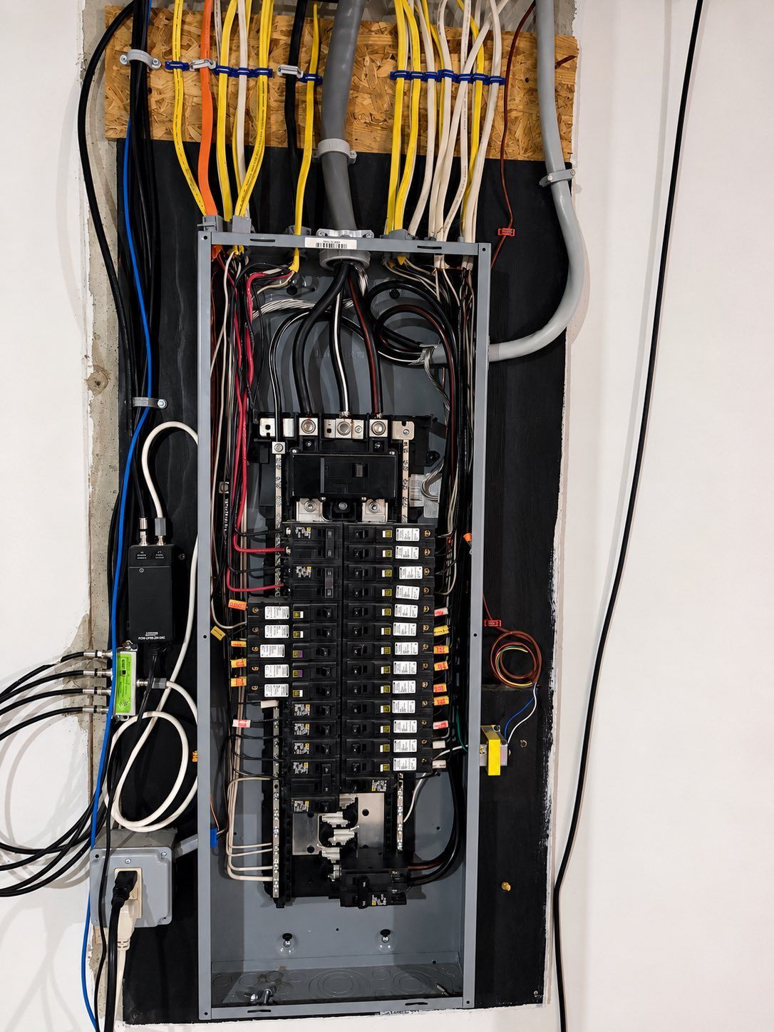 Open electrical panel with exposed wiring and circuit breakers in a wall recess