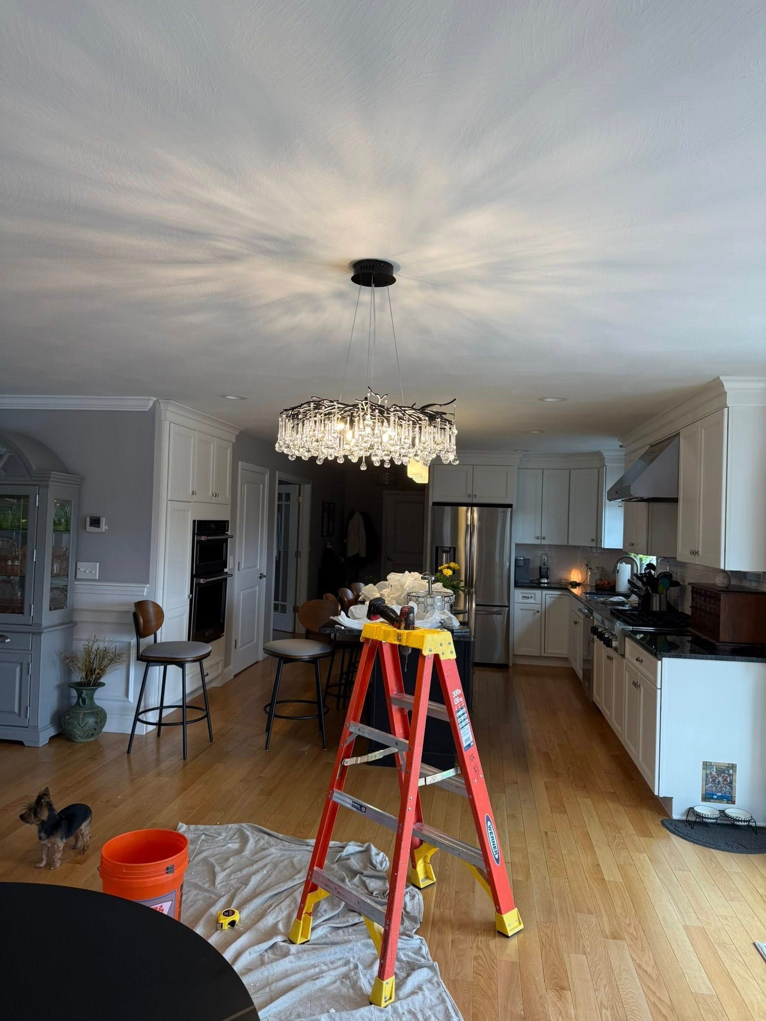 Living room with ladder, tools, and ceiling fixture being repaired
