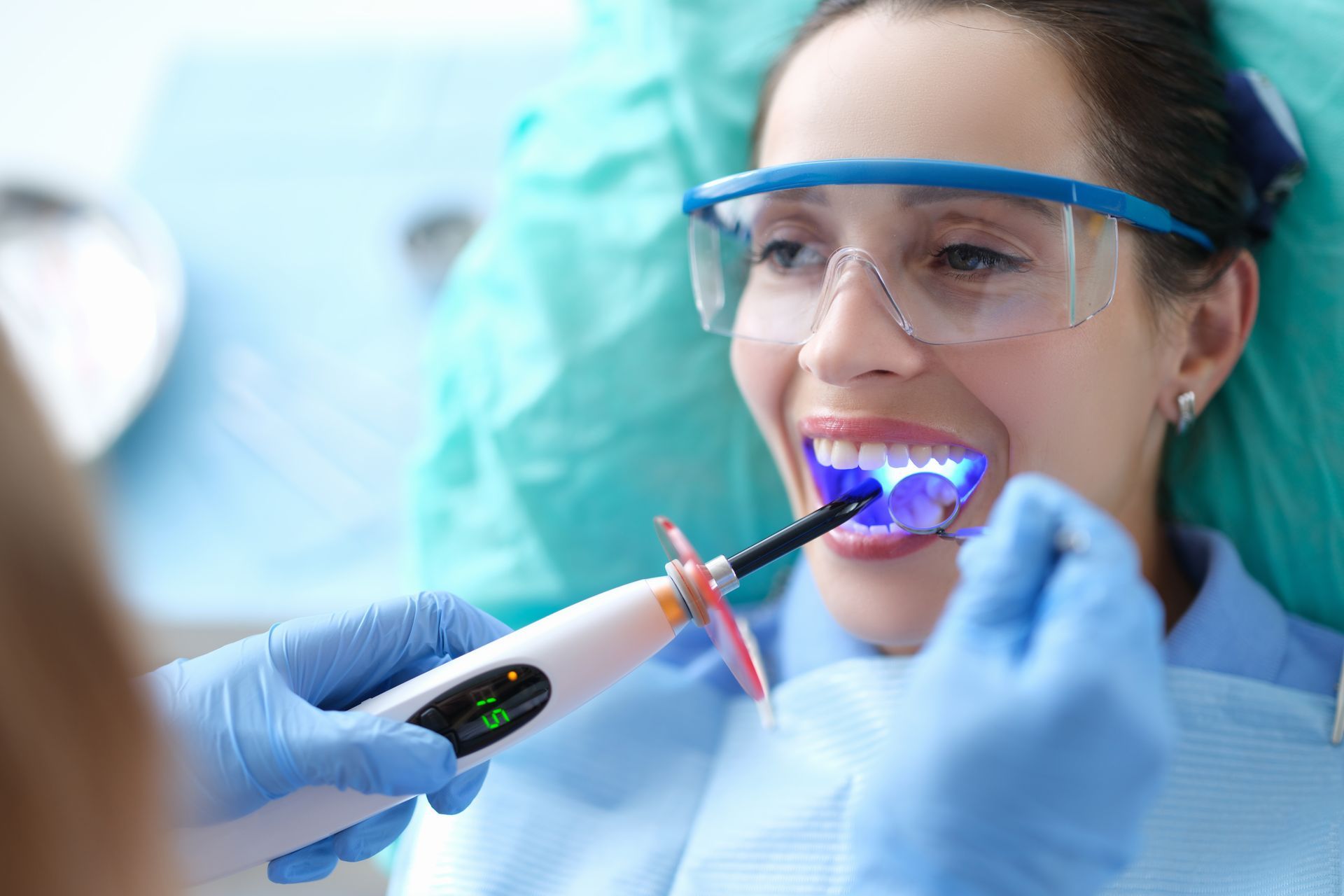 A dentist wearing a white coat uses a pointer to explain a plastic model of human teeth to a patient in an office.