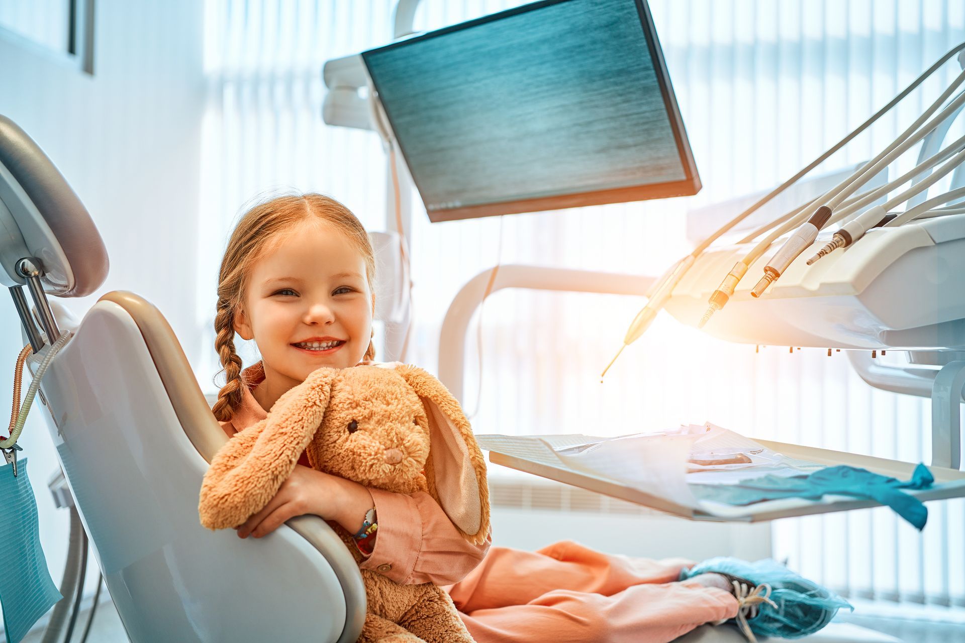 A smiling dentist in a white coat with arms crossed, sitting in a dental office.