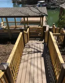 A wooden deck with railings overlooks a backyard with autumn trees and a small white shed under a clear blue sky.