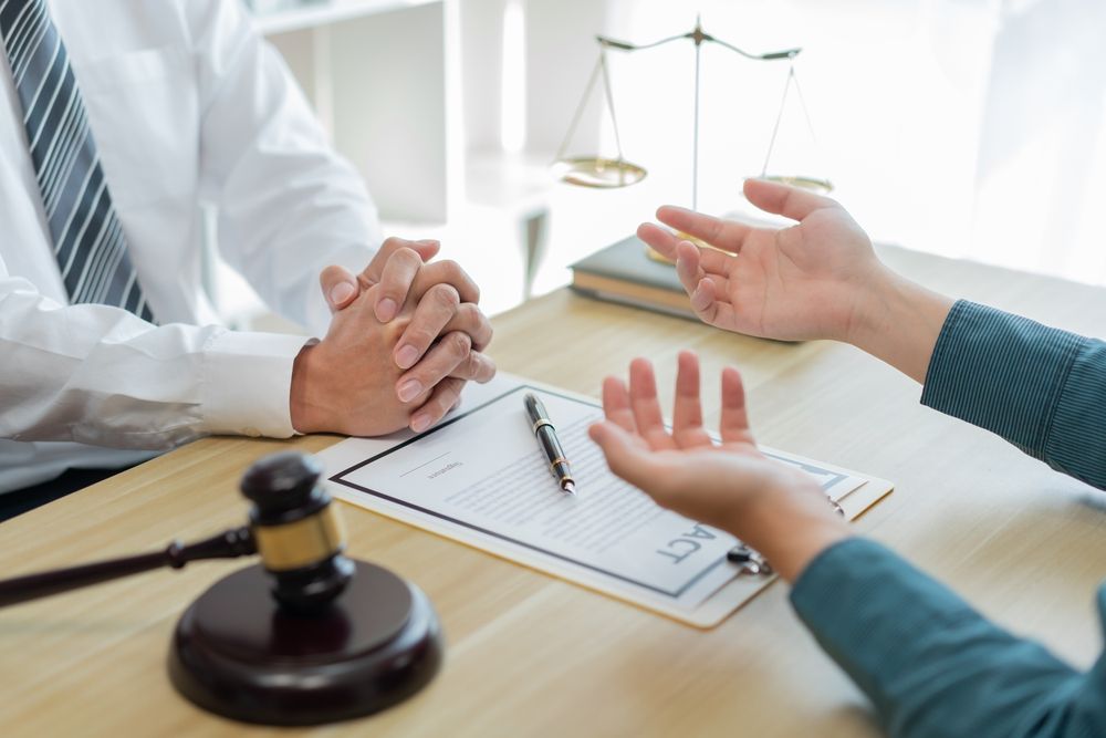Hands in a legal consultation over documents, with a gavel and scales of justice on the table.