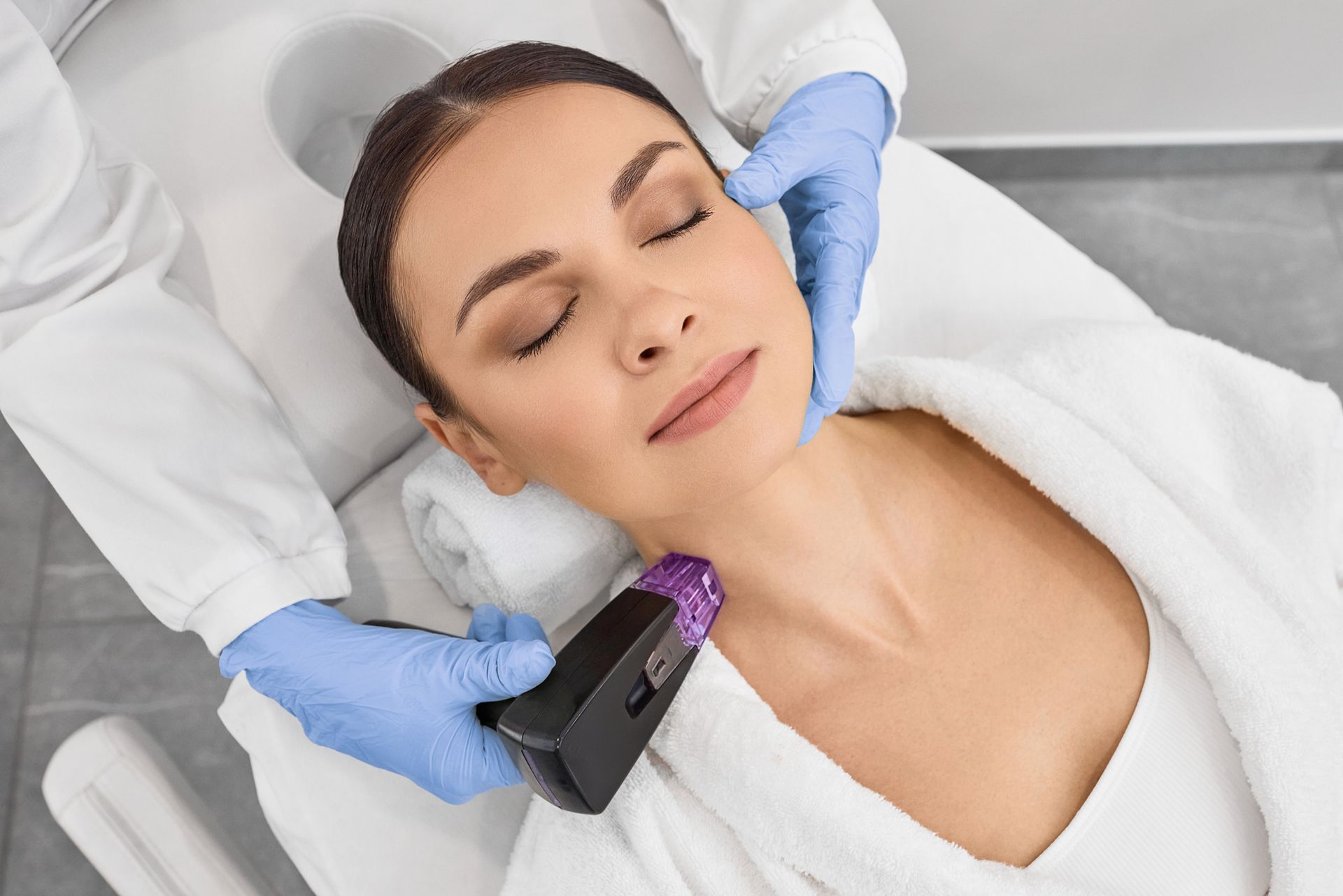 Woman receiving neck treatment at a clinic. Hands in blue gloves hold a device near her neck.