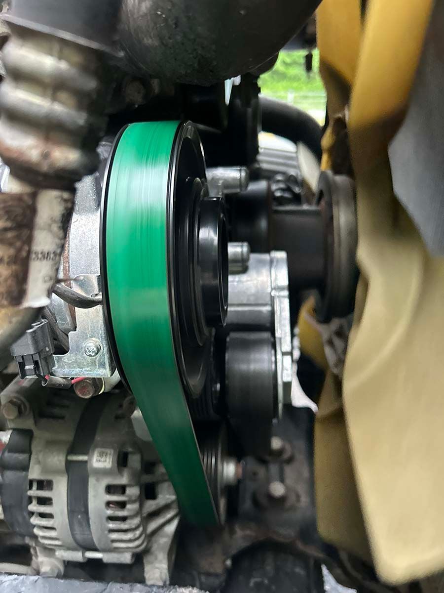 Close-up of a car engine belt and pulley system with a green belt and beige fan blades