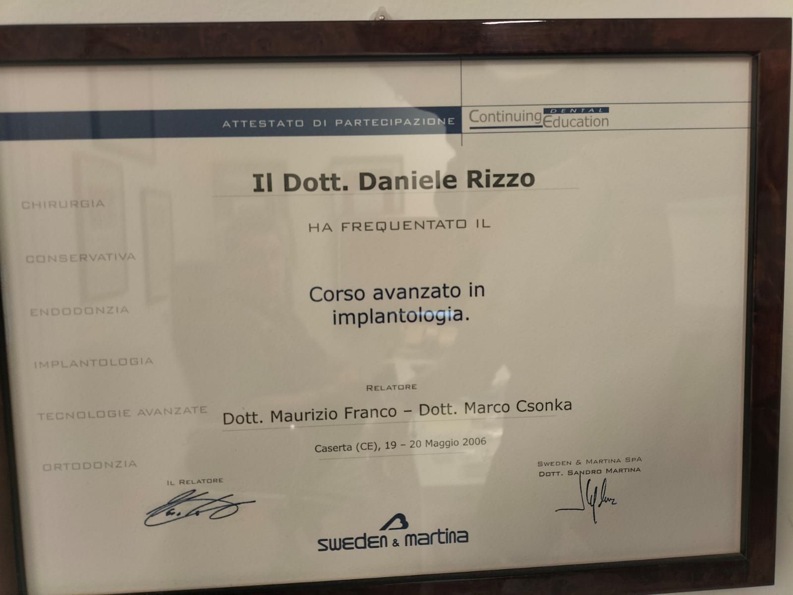 Un certificato italiano incorniciato, appeso al muro, con testo e firme stampati.