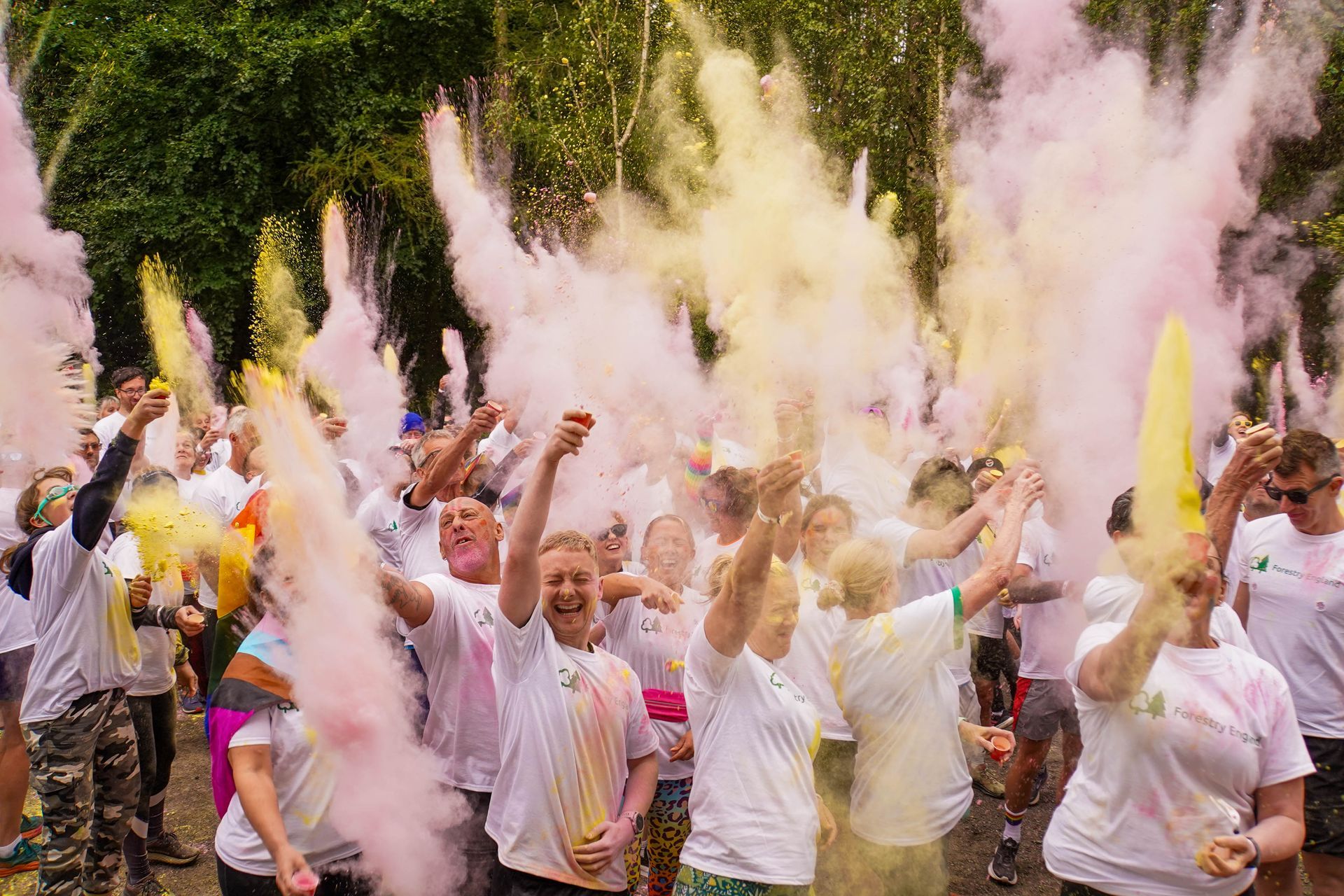 People in white shirts throw colorful powder in the air during a fun run.