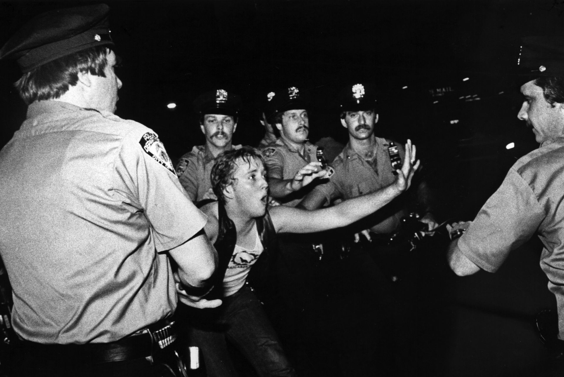 Police officers restrain a struggling person, night scene.