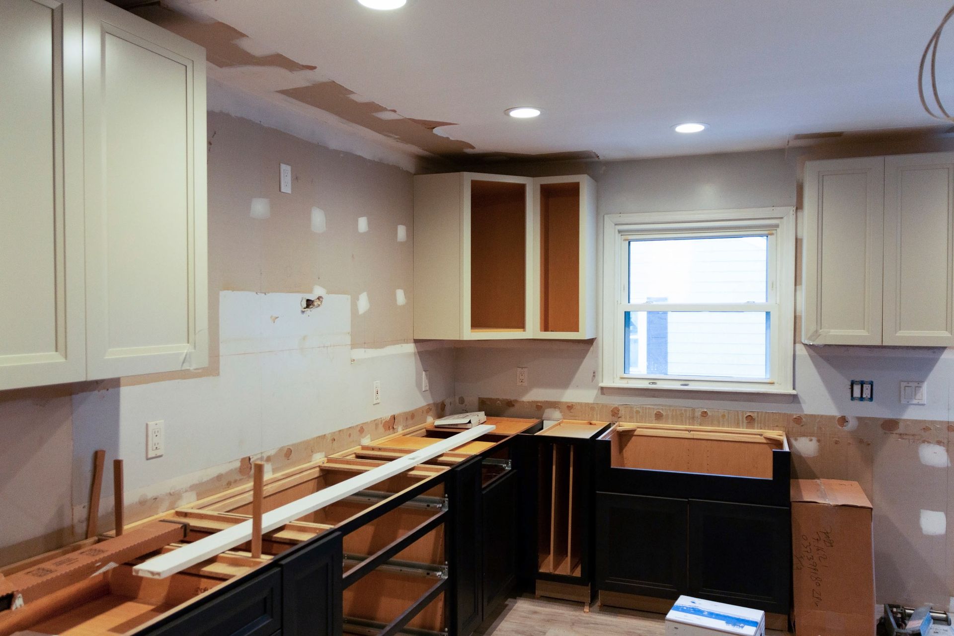 A kitchen under construction with white cabinets and black counter tops.
