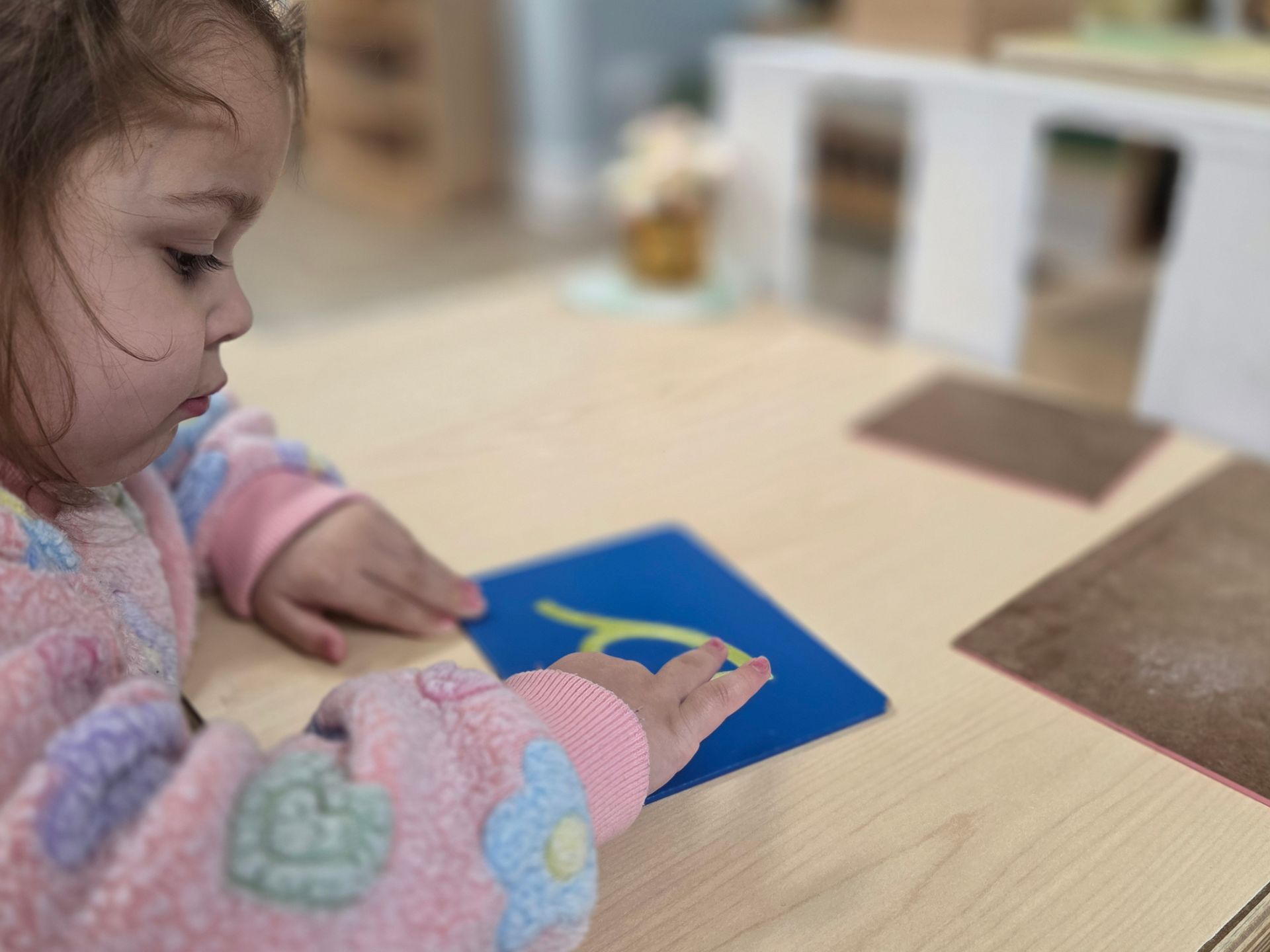 Child tracing a sandpaper letter at a wooden table