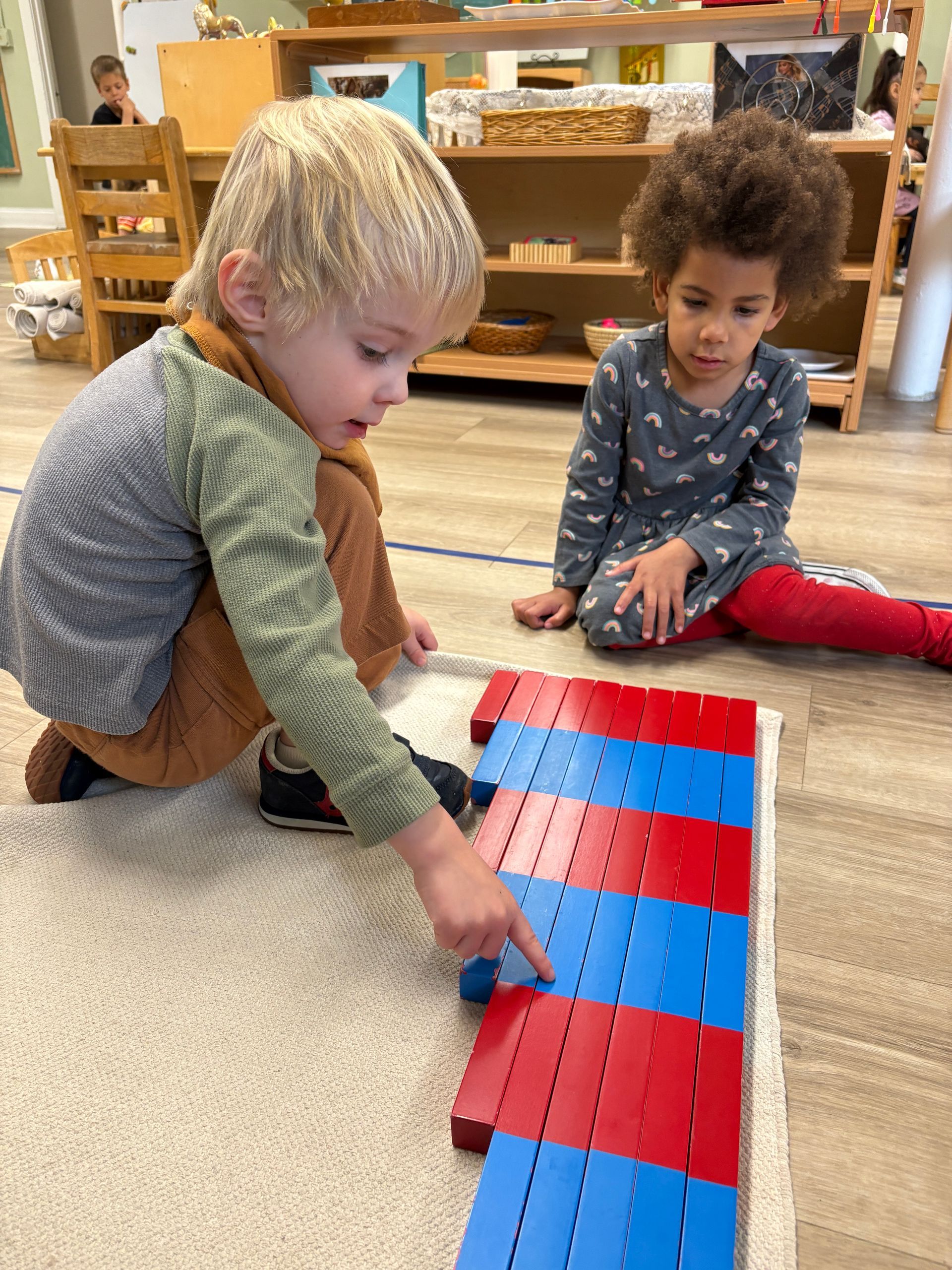 Two children work with the number rods on the floor in a classroom.