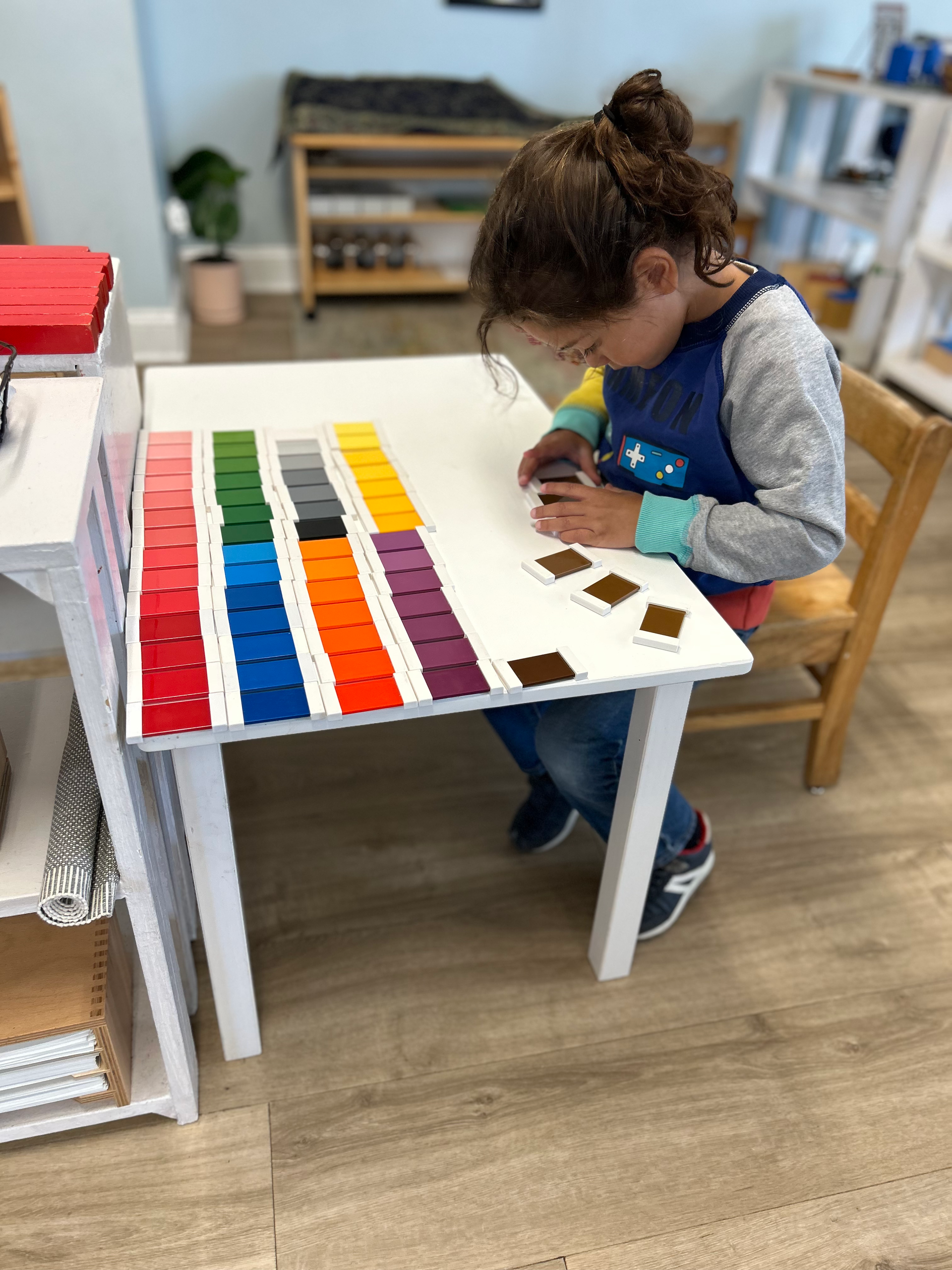 Child arranging color tablets at a small table in a classroom.