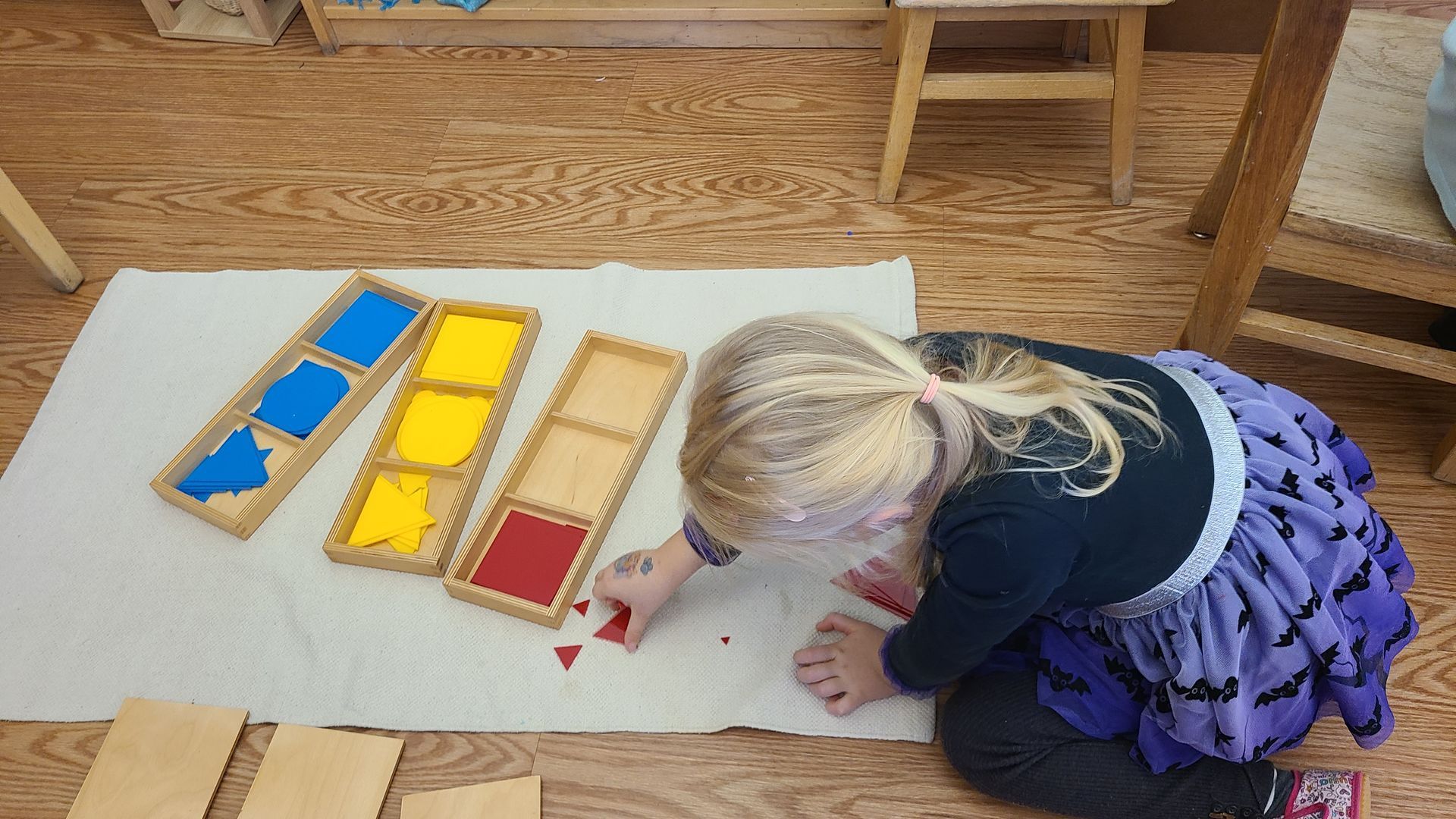 Child kneeling on a rug beside Montessori-style colored blocks in a classroom.