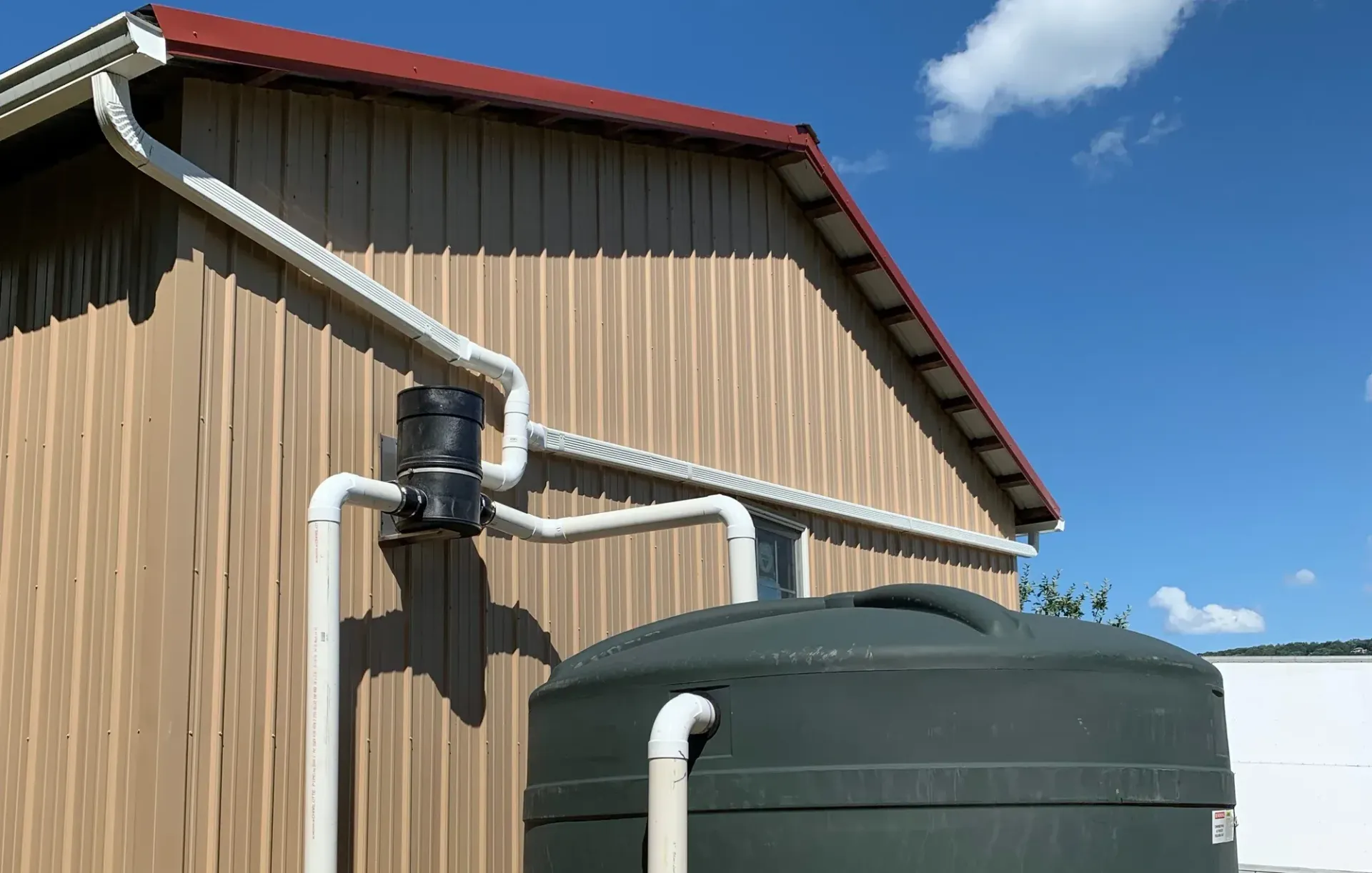 Rainwater flows from a dark gutter into a black barrel.