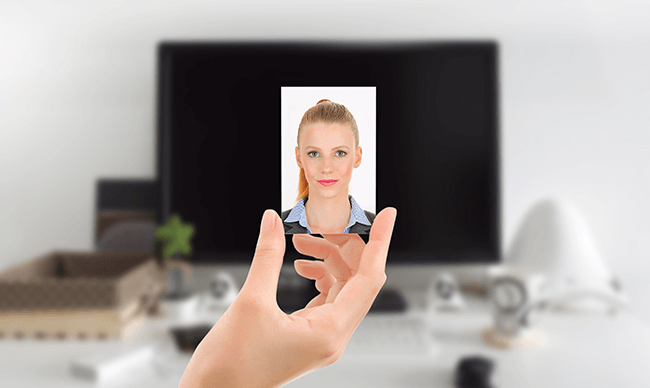 Hand holding a picture showing a woman’s portrait in front of a laptop on a desk