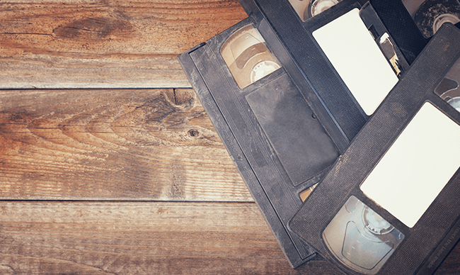 Two black VHS tapes on a rustic wooden table with a white note tucked in one tape