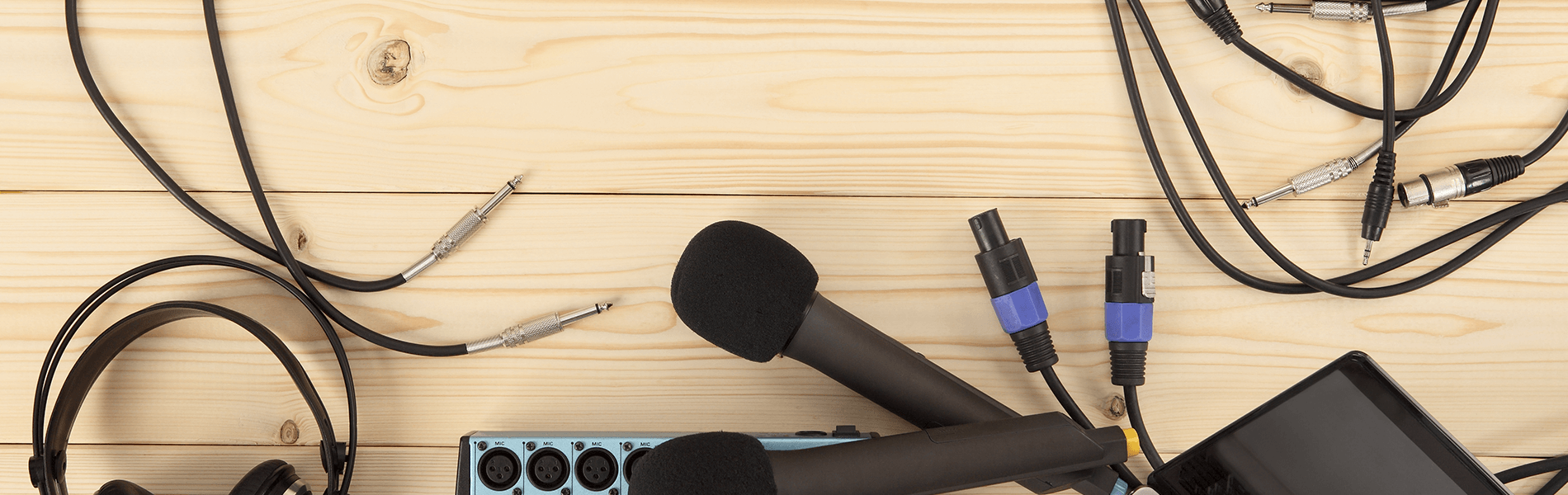 Desk with tangled cables, a black microphone, and audio equipment on a light wood surface