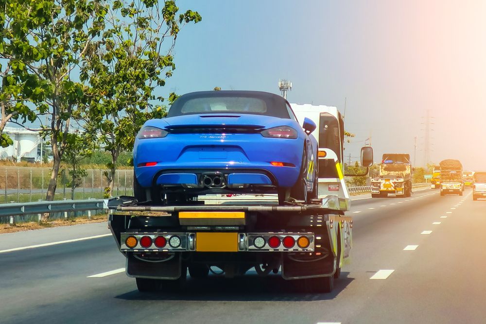 A Blue Sports Car Is Being Towed Down A Highway By A Tow Truck — Alice Hosetech & Industrial Supplies in Ciccone, NT