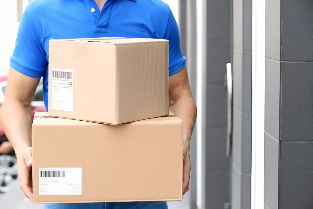 A Delivery Man Is Holding A Stack Of Boxes In His Hands — CC Couriers FNQ in Portsmith, QLD