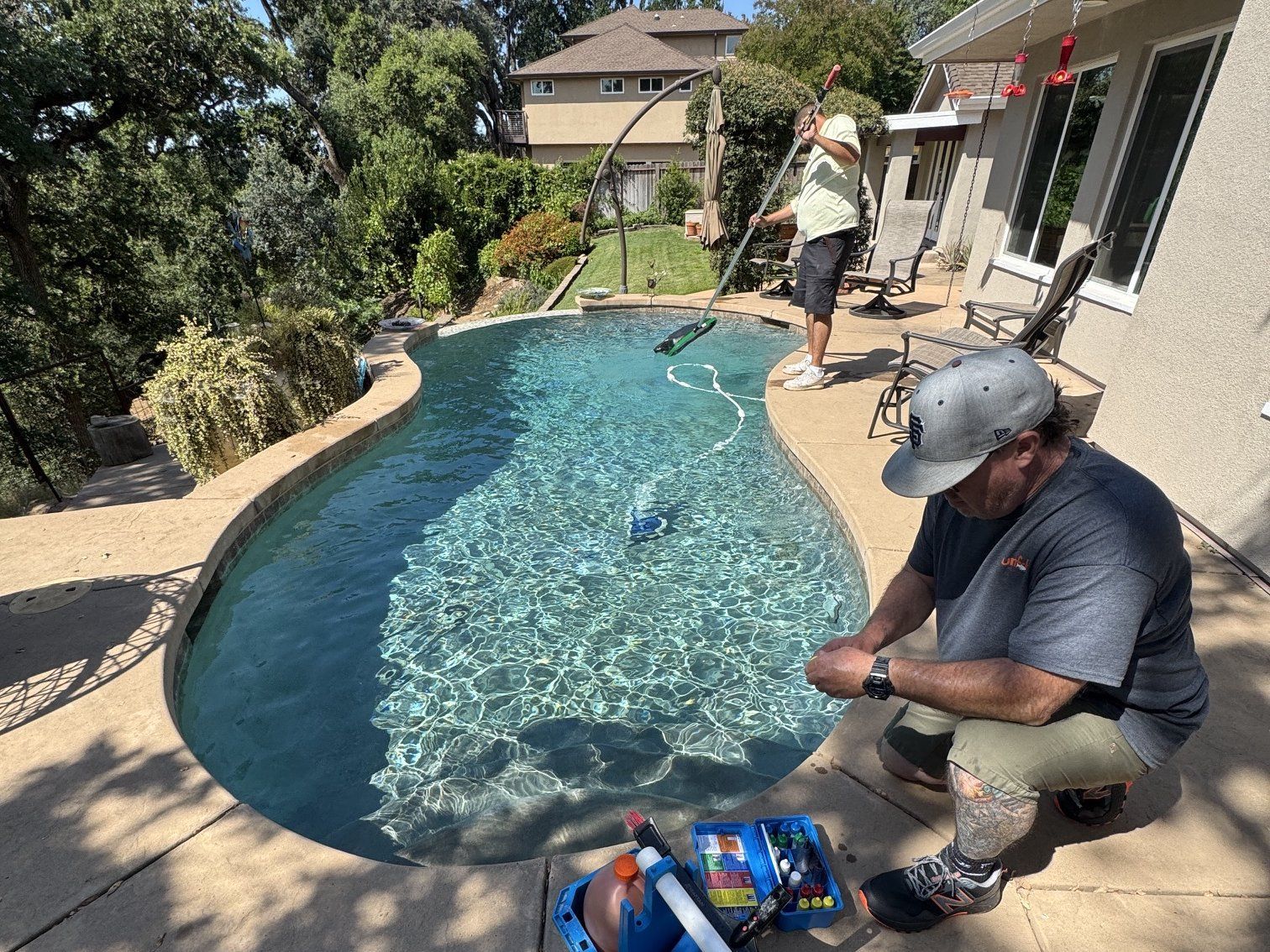 Two Sunfish Pool Service techs testing water and brushing a backyard pool in the Sacramento area