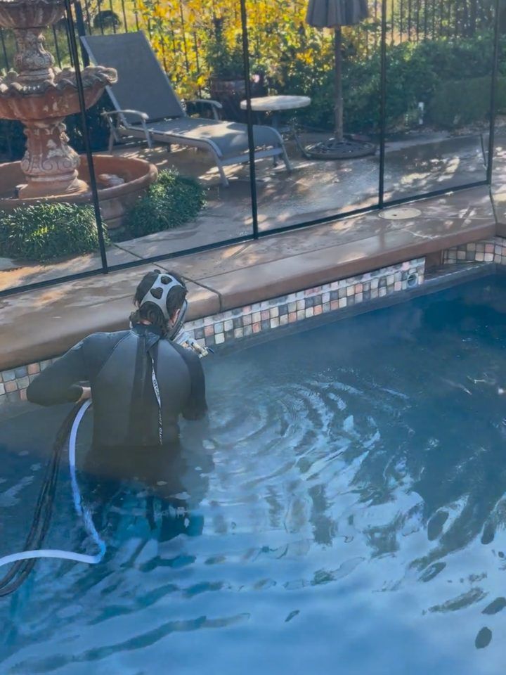 Technician standing in a pool blasting calcium off mosaic waterline tile