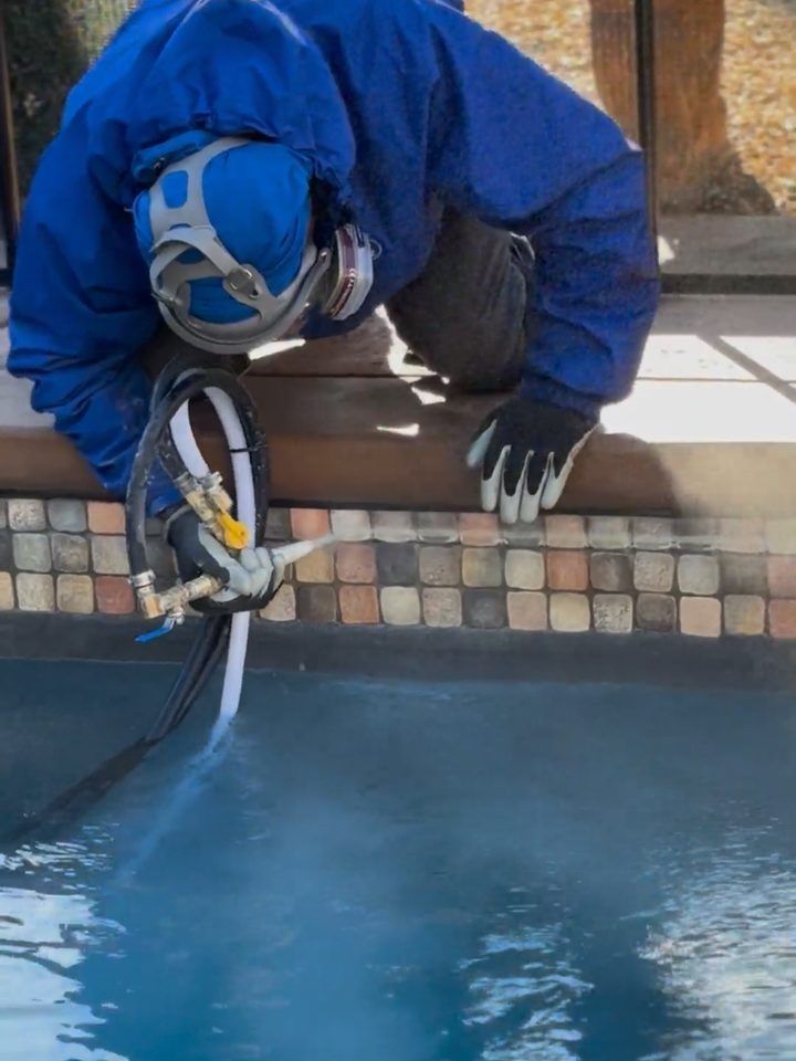 Technician in a respirator and gloves glass bead blasting mosaic waterline pool tile from the deck