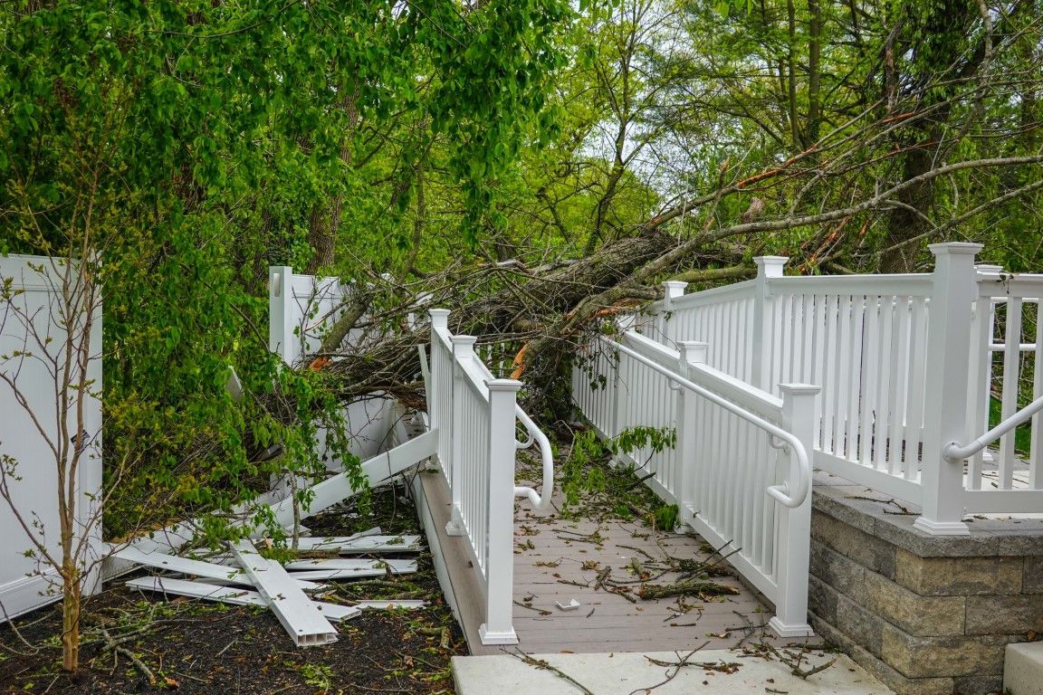 Man in a boom crane cutting a tree that has fallen on top of a house in a forested yard