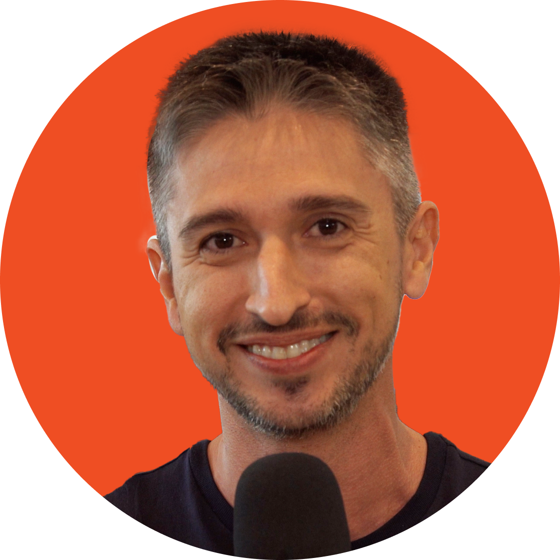 Pessoa sorridente em frente a um fundo laranja, falando ao microfone.