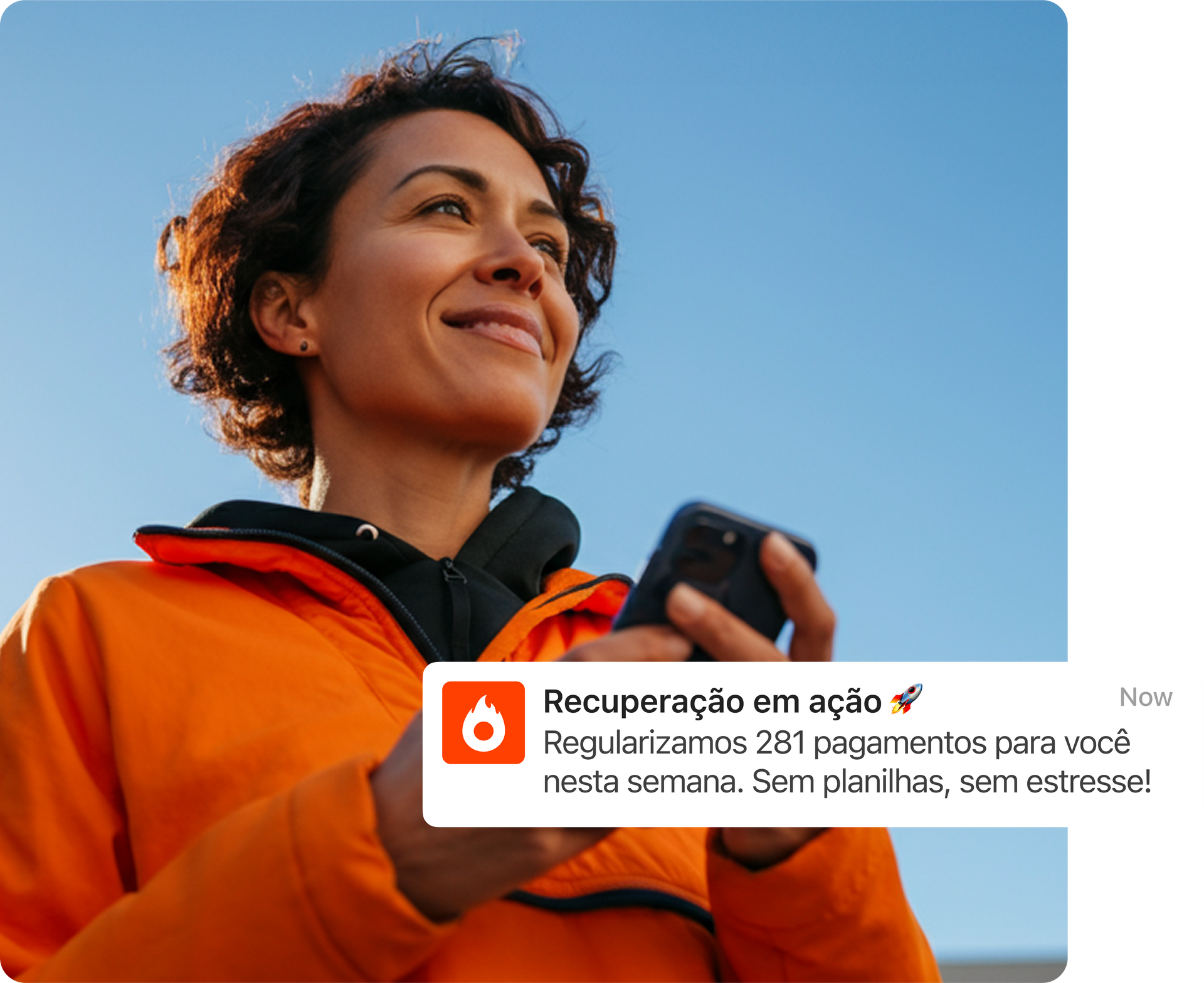Mulher com jaqueta laranja sorrindo ao ar livre enquanto segura um smartphone sob um céu azul.