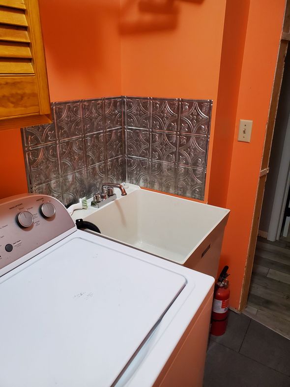Laundry room with white appliances, orange walls, and a utility sink with a tin backsplash.