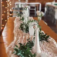 Long banquet table with white floral and greenery centerpiece in a warmly lit room