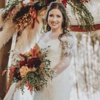 Smiling bride in a white dress holding a fall bouquet under floral wedding decor