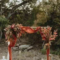 Flower-decorated wooden arch with red drapes in an outdoor wooded setting