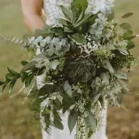 White floral bouquet with greenery against a blurred outdoor background