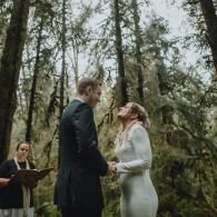 Couple exchanging vows in a forest ceremony, with an officiant nearby.