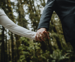 Two people holding hands in a forest, one in a light sleeve and one in a dark suit