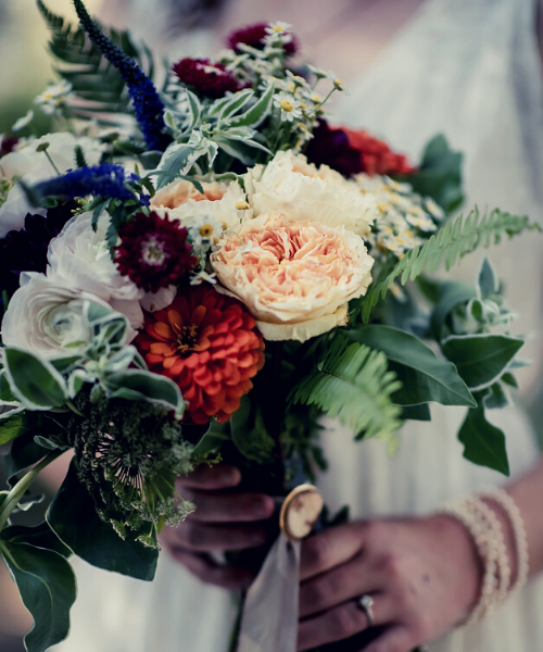 Hand holding a colorful bouquet with cream, red, and purple flowers and greenery