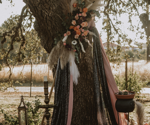 Floral wreath on a tree trunk with draped ribbons in a rustic outdoor setting