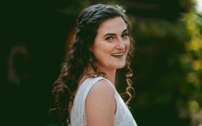 Smiling woman in a white sleeveless top looking over her shoulder outdoors