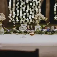 Elegant table centerpiece with flowers, candles, and glassware against soft string lights