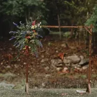 Rustic wooden frame with a hanging bouquet of wildflowers and greenery outdoors