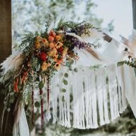 Floral wedding arch with white drapes, greenery, and orange-red flowers outdoors